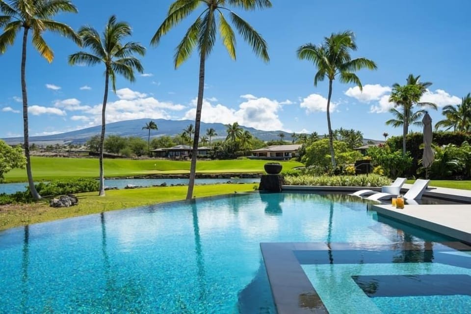 Luxurious infinity pool with swaying palms and mountain views creating the perfect Hawaiian paradise backdrop.