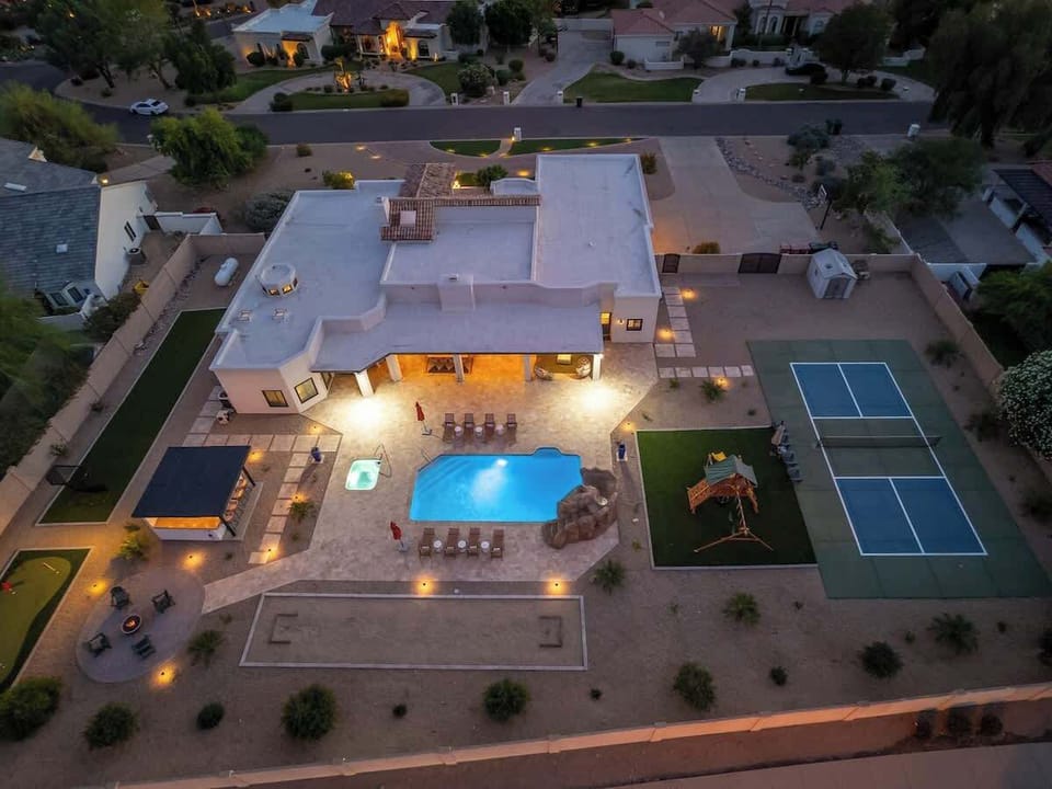Aerial view of a luxury vacation estate featuring a sparkling pool, private tennis court, outdoor entertaining areas, and manicured grounds in an upscale neighborhood.