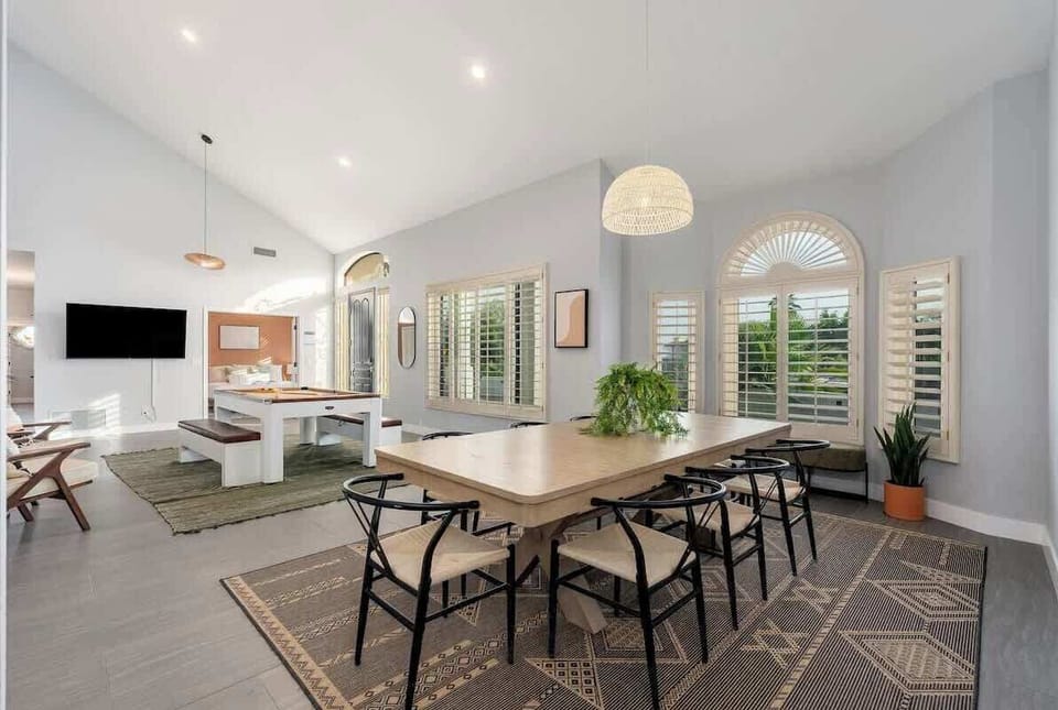 Light-filled open living space blends dining and lounge areas, with high ceilings, elegant shuttered windows, and stylish modern furnishings creating a warm, welcoming retreat.