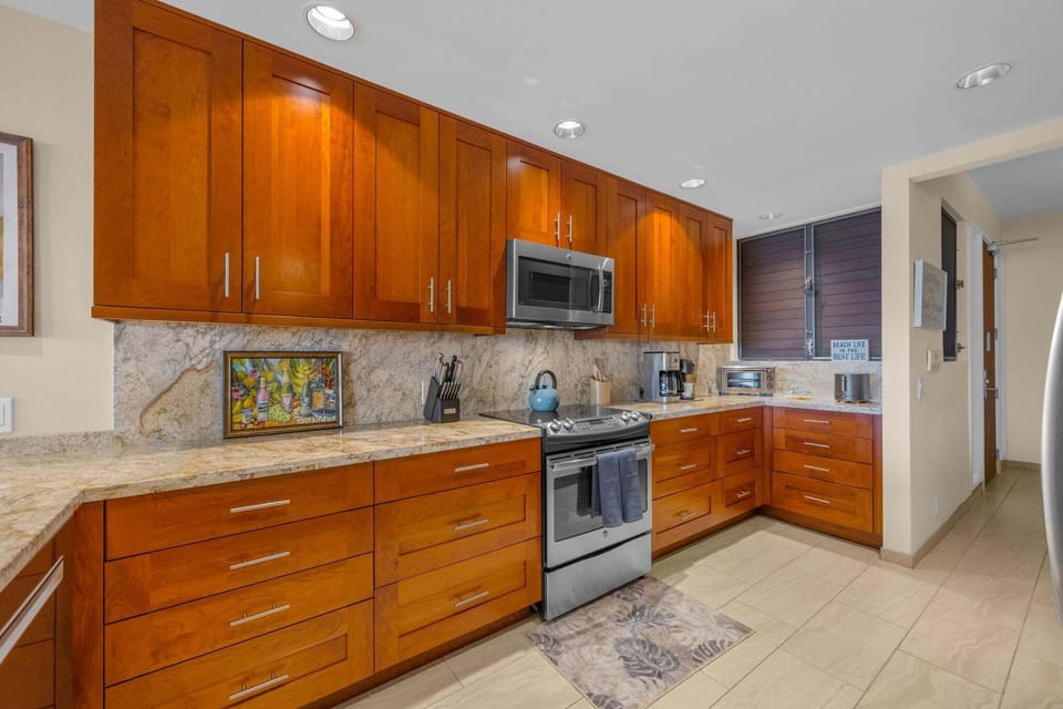 Fully equipped kitchen featuring rich wood cabinetry, granite countertops, a gas stove, and modern stainless appliances.