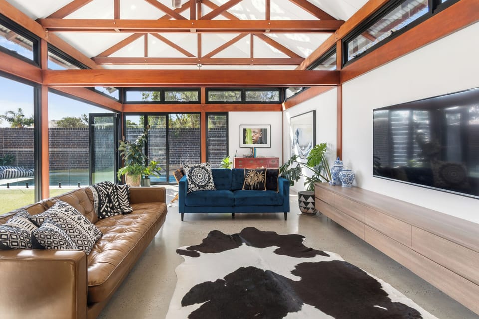 Settle into the leather and velvet sofas beneath exposed timber beams, with the TV ready for evening wind-downs and glass doors opening straight to the pool.