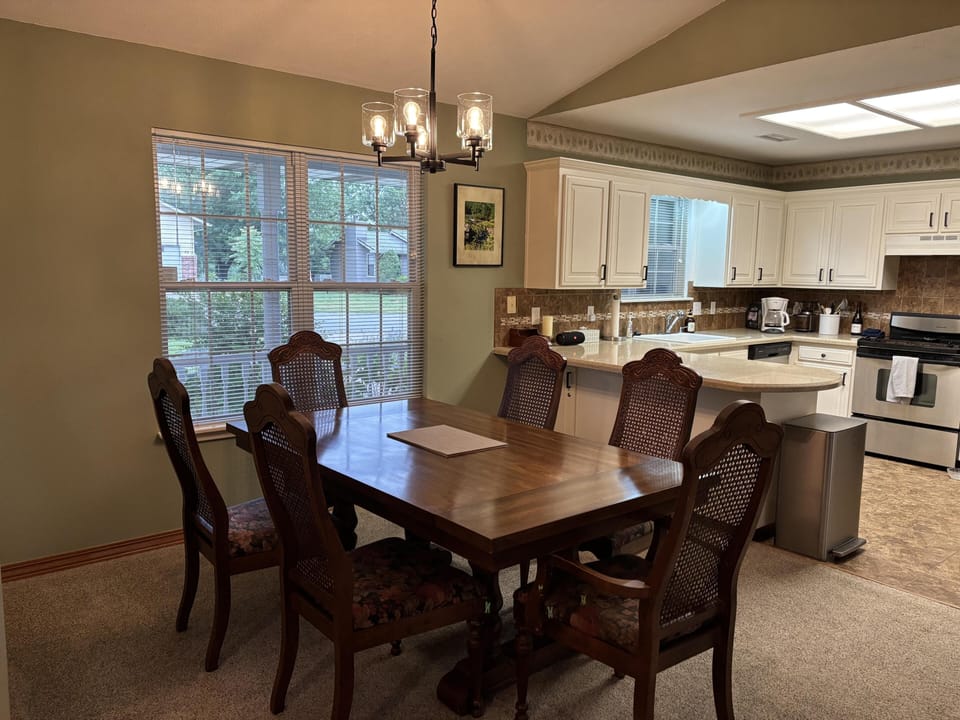 Dark wood dining table with six floral-upholstered chairs beneath a black metal chandelier near kitchen peninsula.