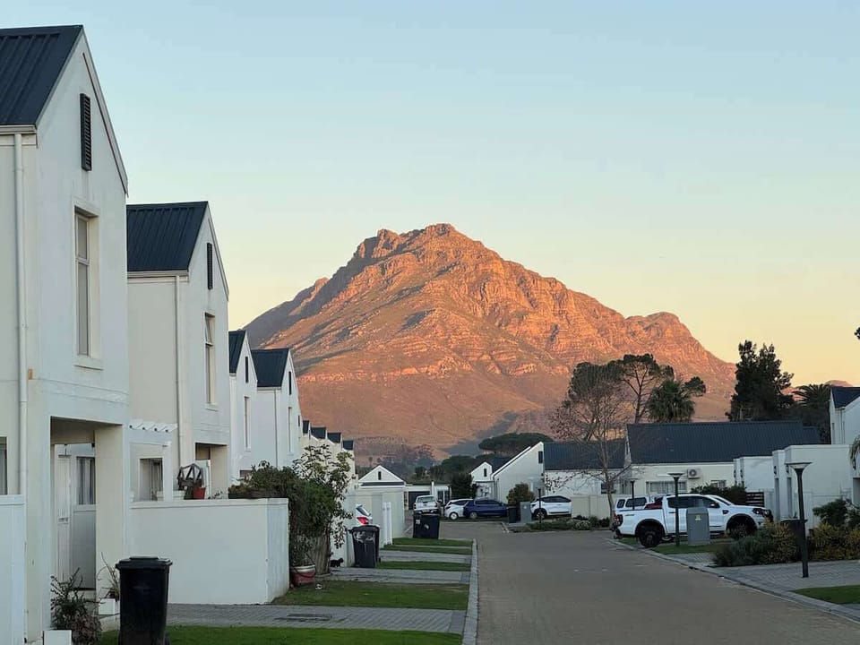 Twilight estate street view with Cape mountain backdrop glowing amber at sunset — that view is free every evening