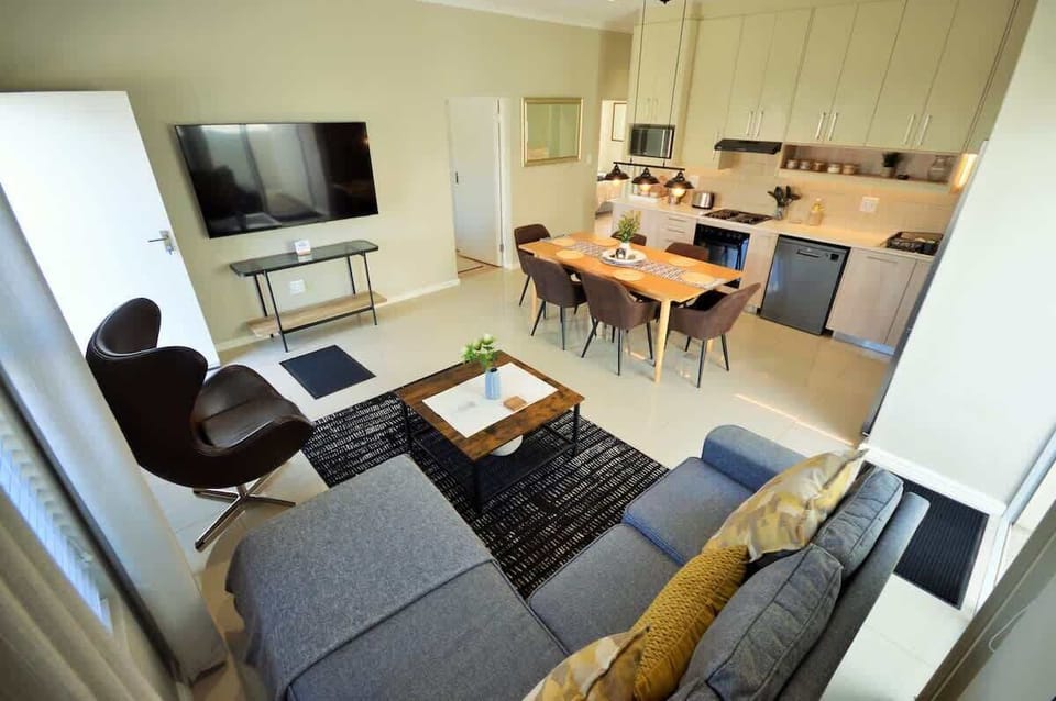 Bright open-plan living, dining for 6, and kitchen with stainless appliances, wall-mounted TV, and egg chair — the social heart of the home