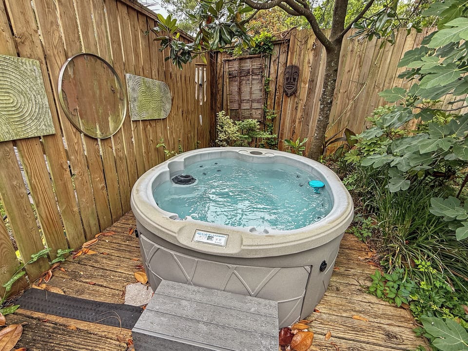 Outdoor hot tub surrounded by lush greenery and rustic fencing