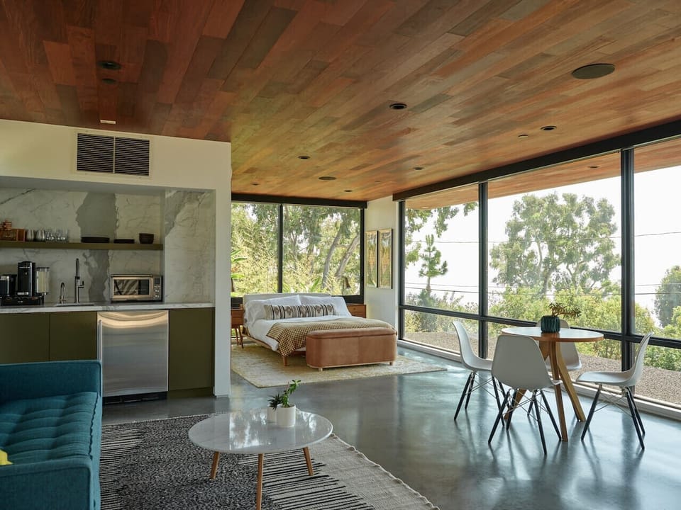 Sunlit mid-century studio with soaring wood ceilings, floor-to-ceiling windows, and lush treetop views - your perfect modern escape.