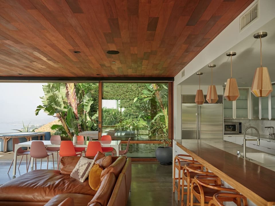 Wood pendants, a teak island, and banana palms framing the view. Cooking never looked this good.