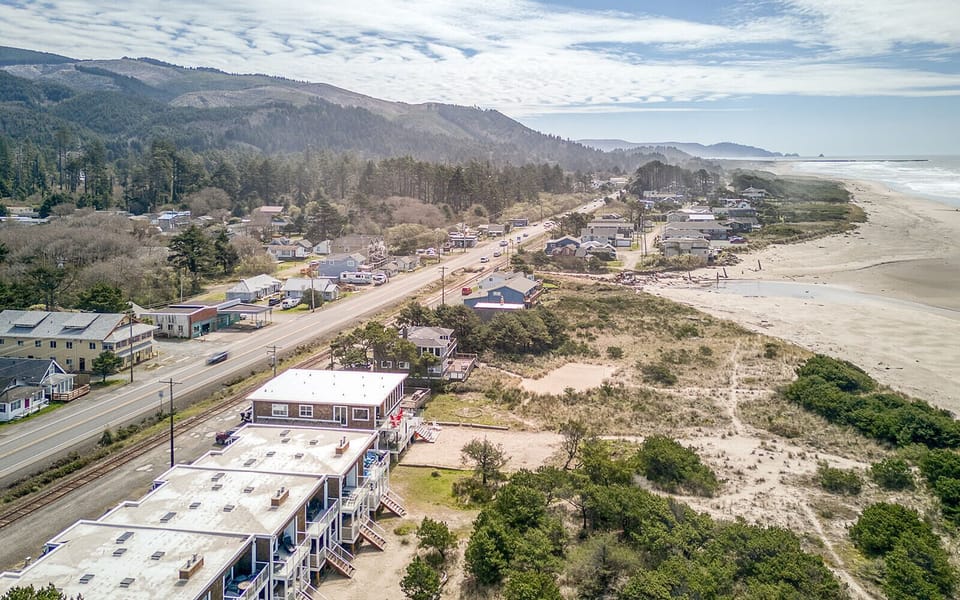 Coastal community nestled between rolling hills and pristine beach, with scenic highway connecting mountain forests to ocean shores.