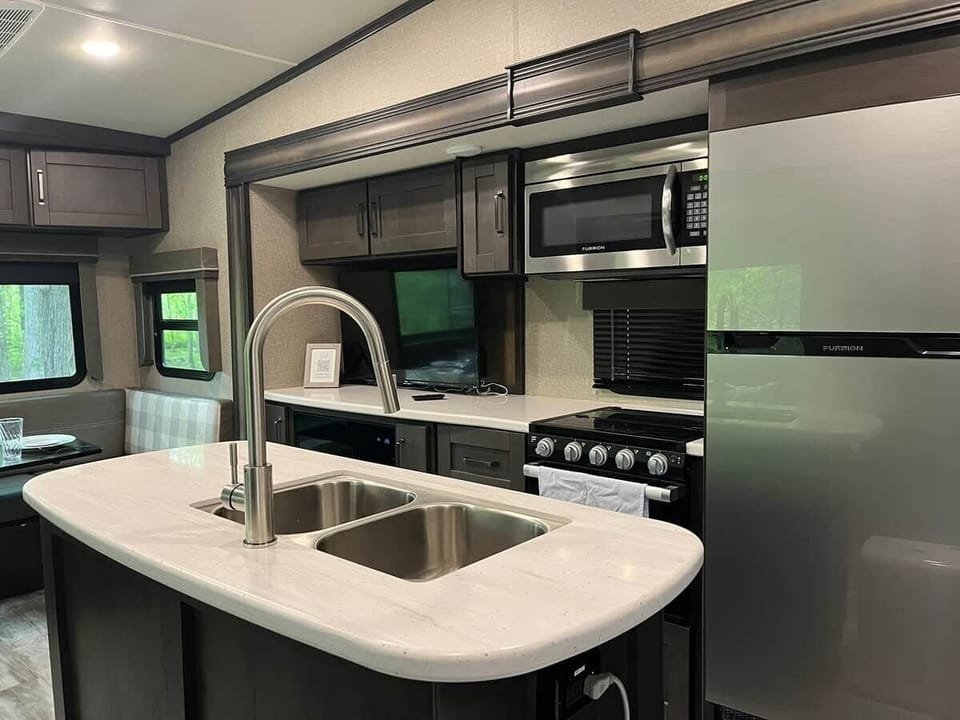 Equipped RV kitchen with sink, stove, refrigerator, and wooded views