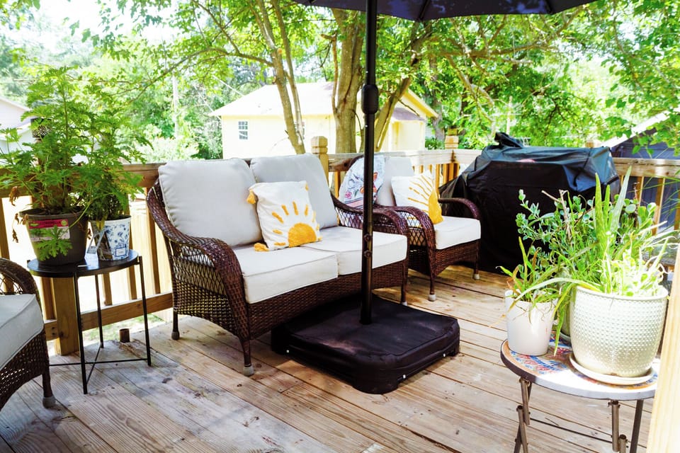 Private shaded deck with cozy seating, lush greenery, and outdoor grill