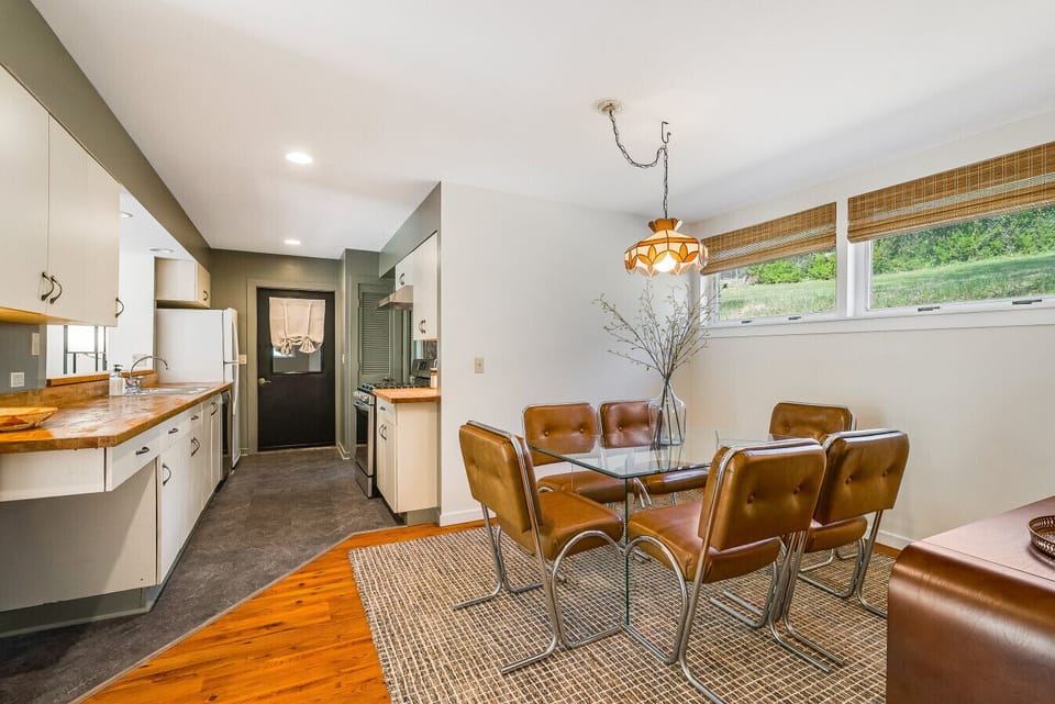 Open-concept dining and kitchen space with beautiful wood-block countertops, vintage-inspired seating, and natural light from wide windows.