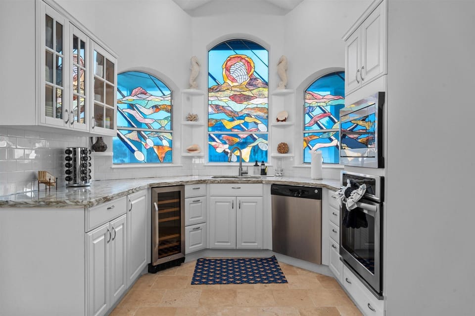 Bright kitchen with custom cabinetry, marble-style countertops, and decorative stained glass windows adding unique coastal charm.