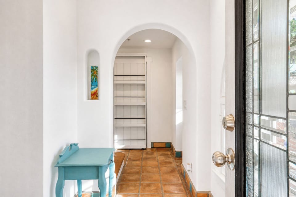 Step into a bright entrance hall with charming white arches, warm terracotta tiles underfoot, and vibrant pops of color welcoming you home.