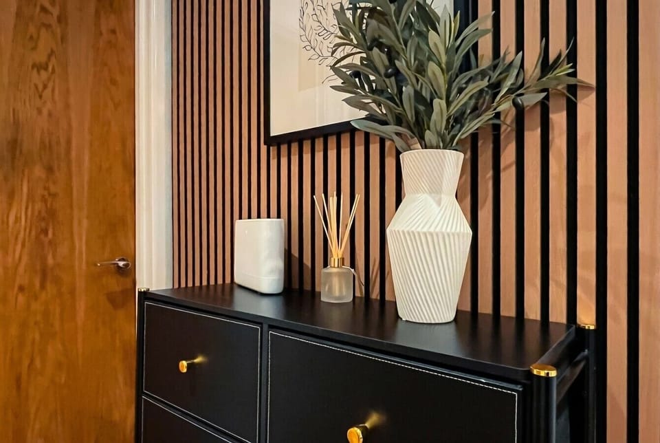 Hallway chest close-up with reed diffuser and fresh plant framed by the signature oak slat wall.