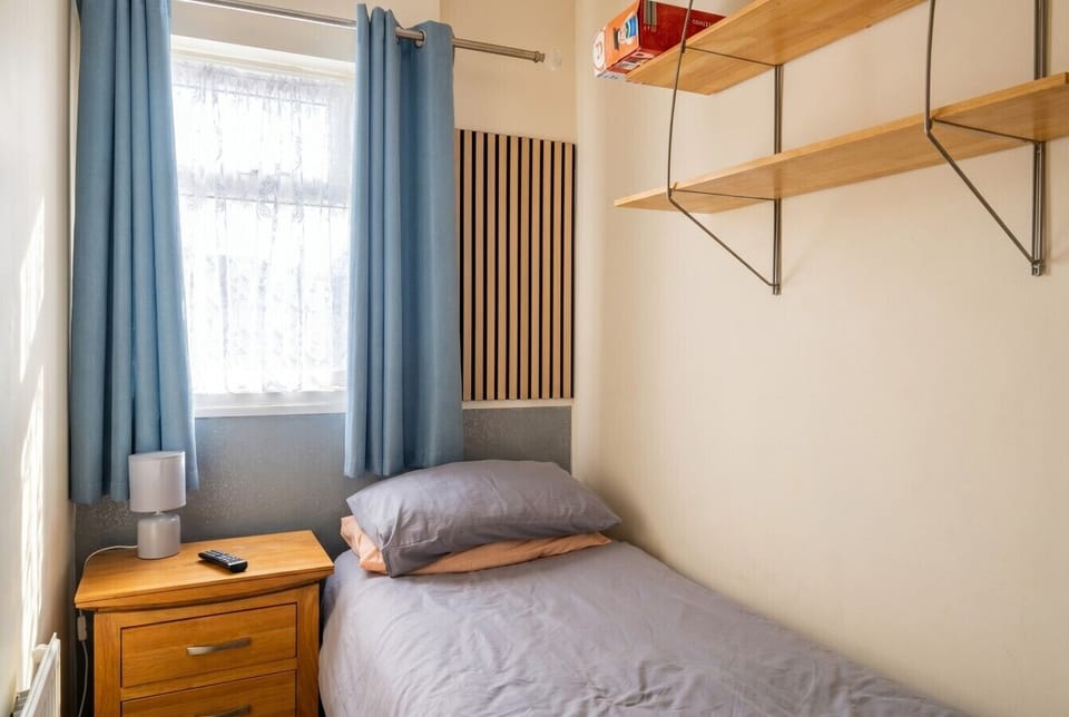 Bright single room with fresh linen, open shelving, and a calming blue colour palette.