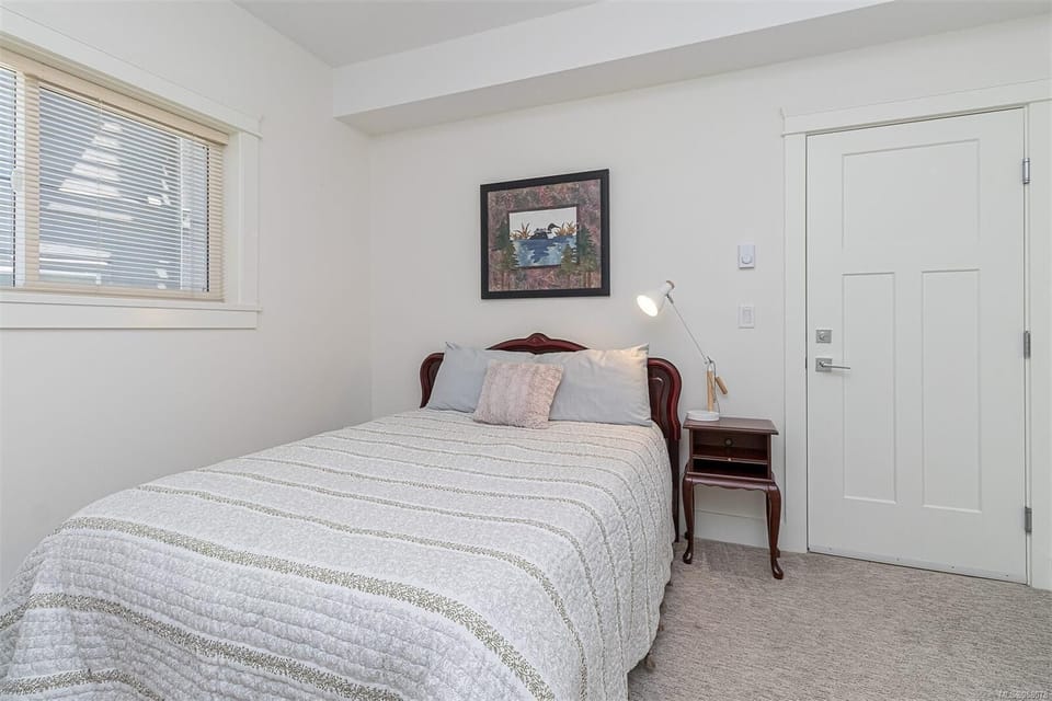 Bedroom with carved wood headboard, striped quilt, plush pillows, and a nightstand lamp by a white door.