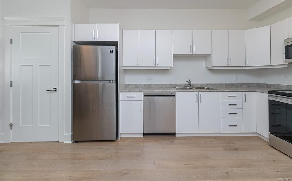 White cabinetry stretches across the kitchen wall with a stainless steel fridge, dishwasher, and light wood flooring.