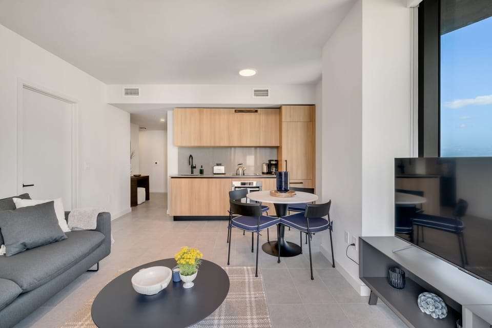 Open-concept layout with TV, dining area, and bright city views.