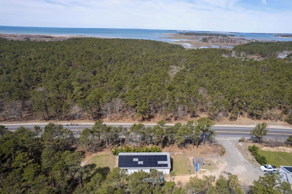 Aerial view of coastal property nestled between forested landscape and ocean access, offering peaceful surroundings near pristine beaches.