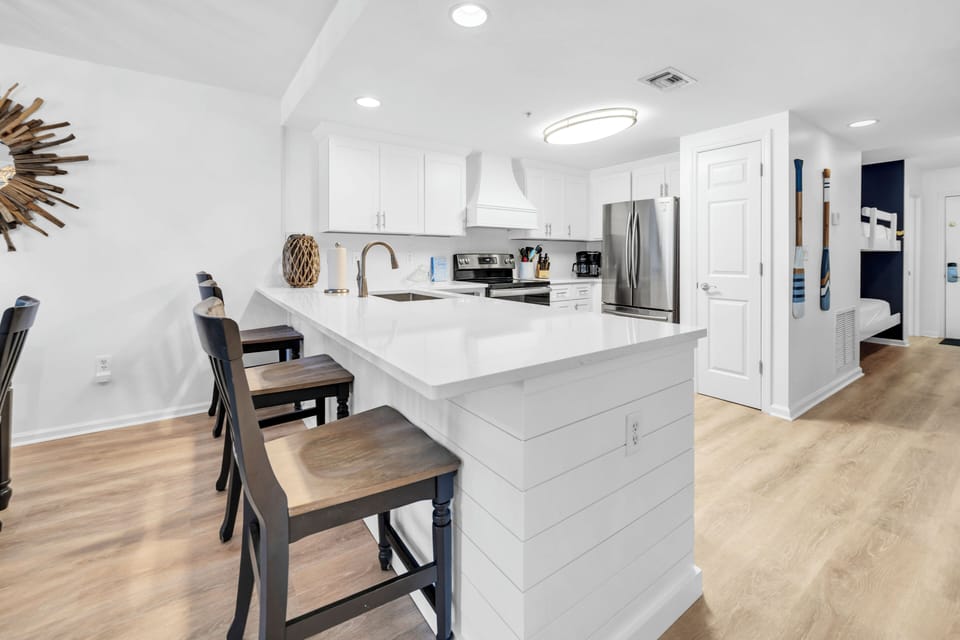 Prepare delicious meals in your spacious, modern kitchen featuring pristine white cabinetry, stainless steel appliances, and a convenient breakfast bar.