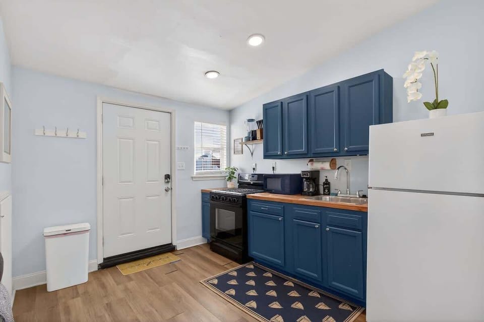 Bright kitchen space with blue cabinetry, essential appliances, and direct access to the entry—designed for convenience and easy meal prep.