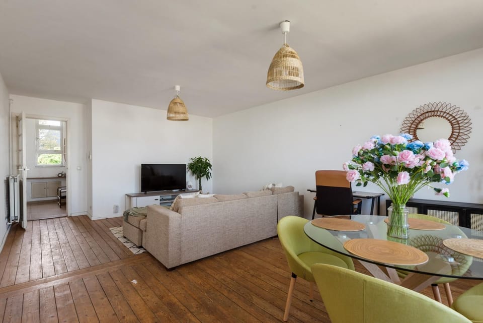 Open living and dining space with wooden floors, comfortable seating, and a TV for relaxed evenings. Large windows bring in natural light while the dining table creates a welcoming spot for meals or casual gatherings.