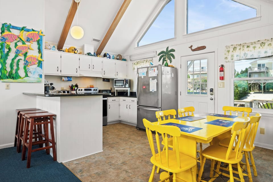 Gather around the cheerful yellow dining table in your fully-equipped kitchen, where coastal charm meets convenience. Sunlight streams through vaulted ceilings as you prepare meals together and plan your next beach adventure.