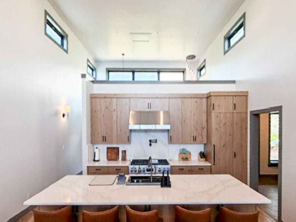 Modern kitchen with quartz island, leather bar seating, and natural wood cabinetry under high ceilings