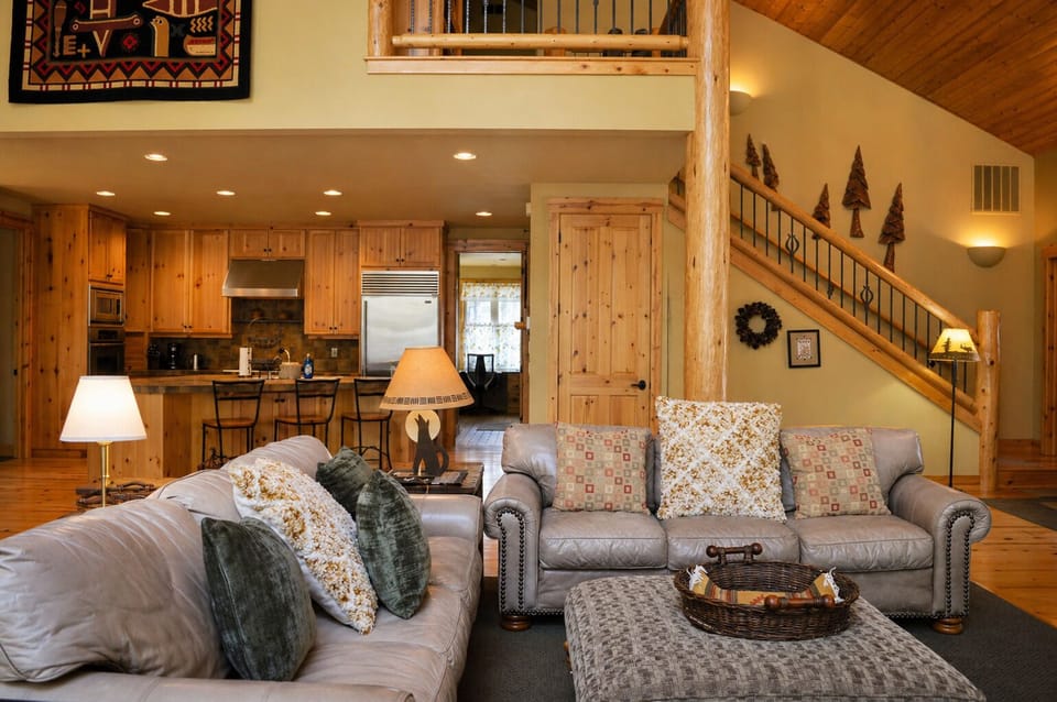 Relax in your cozy living room featuring warm wood accents, plush sofas, and a fully equipped kitchen for memorable mountain getaway moments.