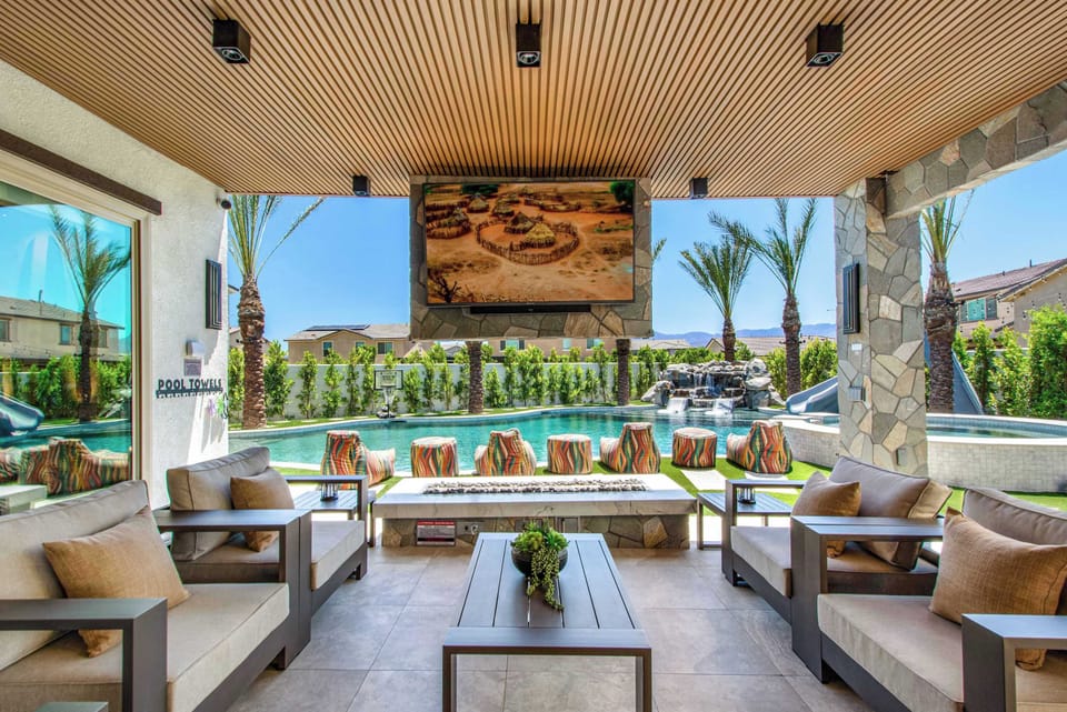 Unwind in the shaded outdoor living room featuring plush seating, a suspended TV, and beautiful pool views. Whether you’re catching the game or enjoying a movie night, this space is designed for relaxing in style.