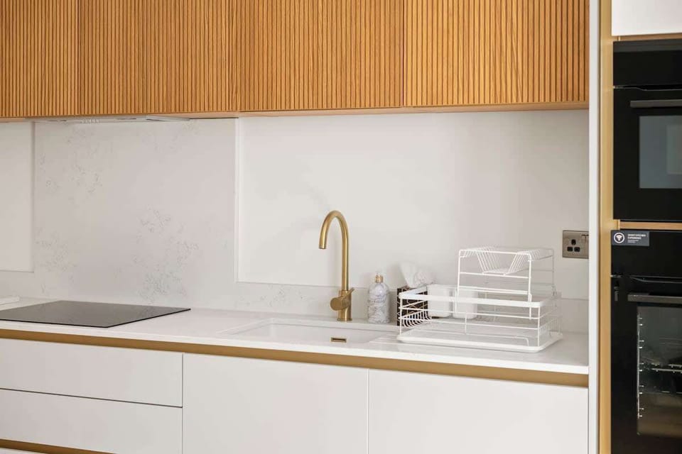 Minimalist kitchen sink area with wooden cabinets and white surfaces
