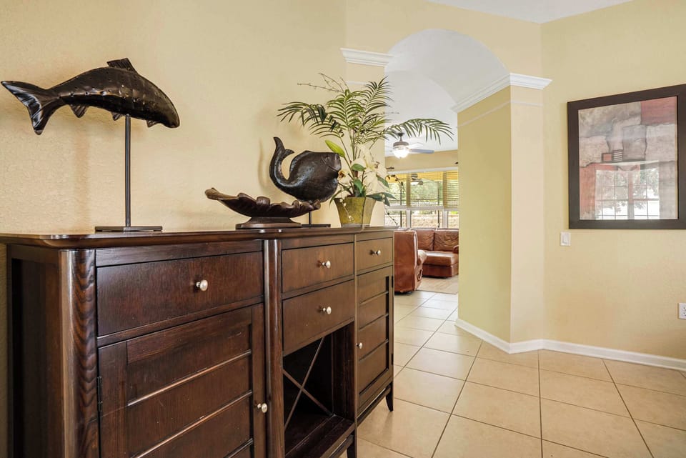 Dark wood cabinet with decorative fish sculptures and a view into the living room through an arched doorway