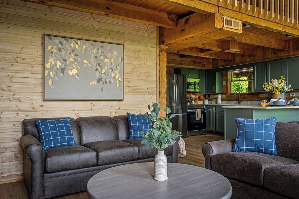 Sink into the leather sectional under gilded leaf art while someone else handles dinner in the green-cabinet kitchen behind you. Open-concept cabin living, done right.