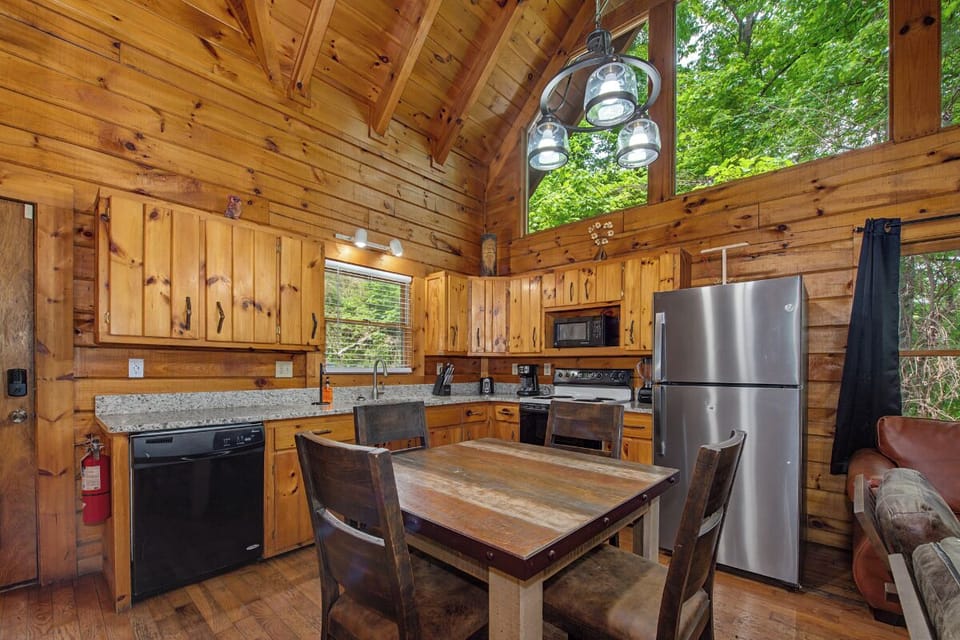 Rustic wood surrounds you in this open kitchen and dining space, where vaulted ceilings and large windows frame views of lush greenery. Gather for meals at the handcrafted table with modern appliances at your fingertips.