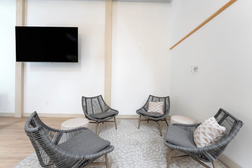 A shared lounge area featuring modern woven chairs and a wall-mounted TV—your perfect spot to unwind with other travelers after exploring the area.
