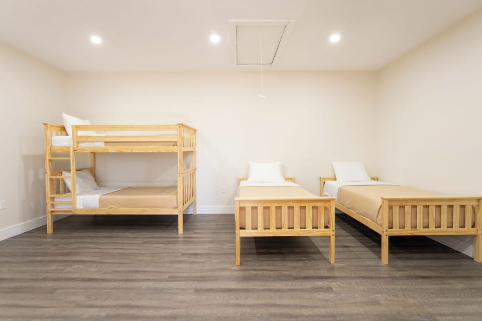 Your spacious bedroom features natural wood furniture and crisp white linens, perfect for families or groups. The bunk bed and twin beds offer flexible sleeping arrangements in a bright, peaceful setting.