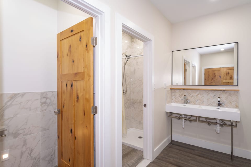 Modern spa-inspired bathroom with elegant marble tilework, spacious walk-in shower, and dual vanity for your comfort. Rustic wooden doors add warmth to the sophisticated design.