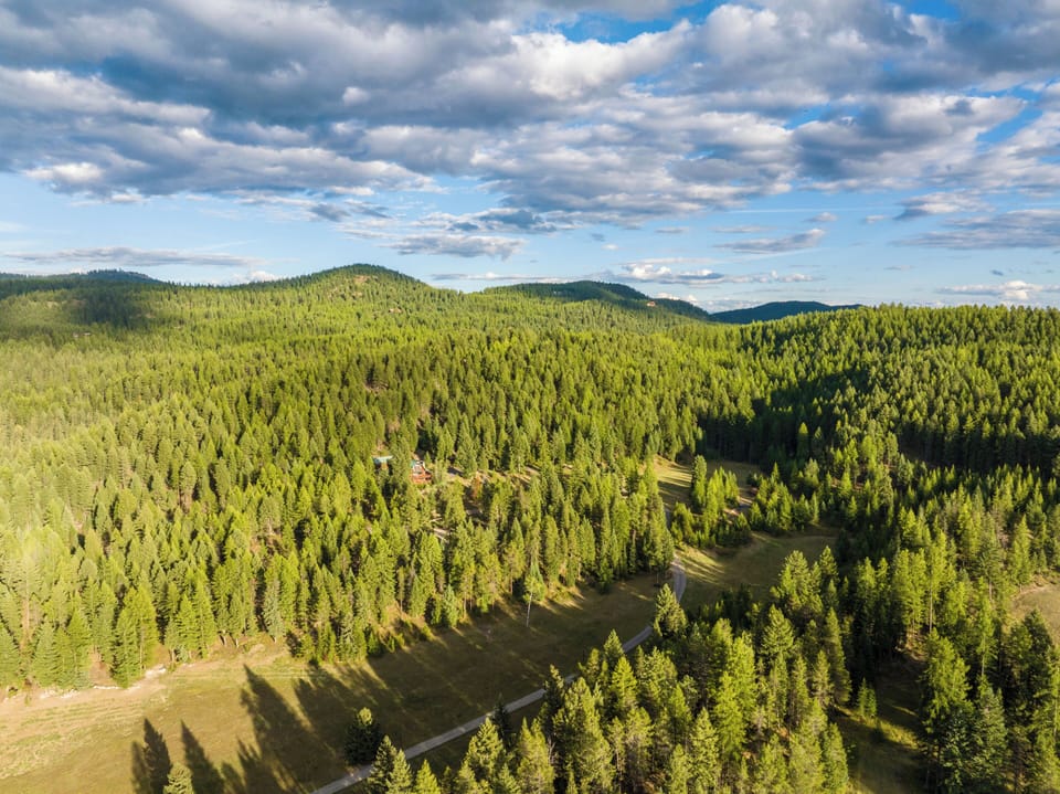 Stunning aerial view showcases vast forested mountains and rolling hills surrounding the property area.