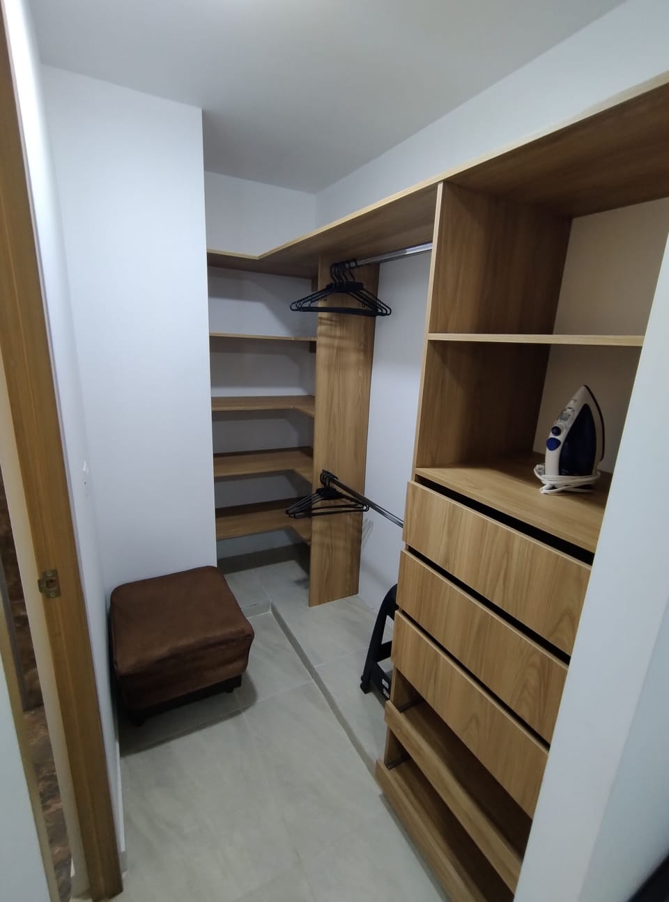 Walk-in closet with shelves, drawers, mirror, iron, and clothes rack.