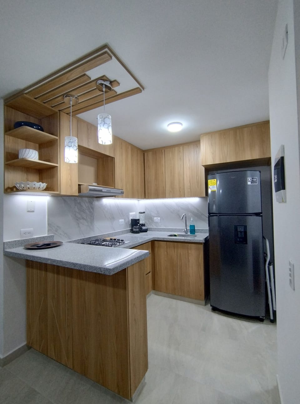 Modern kitchen with fridge, stove, coffee maker, and warm wood design.