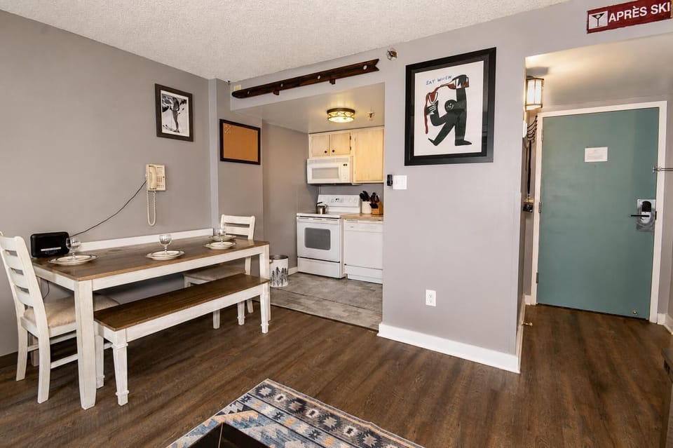 Dining area features a wooden table with bench seating, set against gray walls and dark hardwood floors.