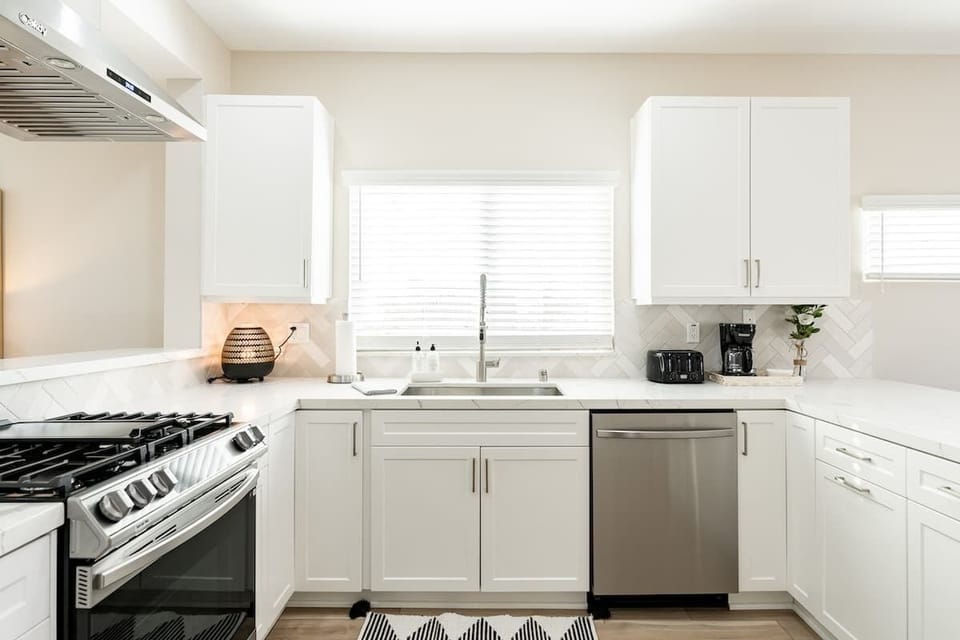This bright and modern kitchen features sleek white cabinetry, stainless steel appliances, and ample counter space. The large window brings in natural light, creating an inviting space for cooking and entertaining. ☀️✨