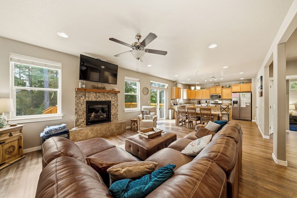 Sink into plush leather sofas in your open-concept living space, warmed by a cozy fireplace and ceiling fan. Large windows frame scenic views while the adjoining kitchen invites shared meals and laughter.