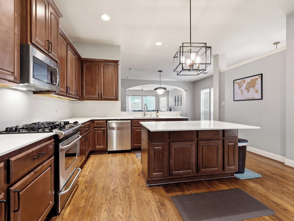Your spacious open-concept kitchen invites you to gather around the central island, where warm wood cabinetry meets modern stainless appliances under elegant pendant lighting—perfect for cooking and connecting.