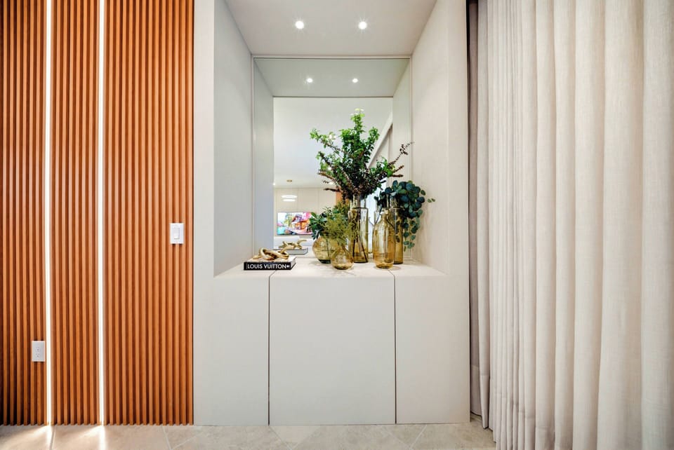 Welcome to a bright entryway with warm wooden accents and sleek white cabinetry, where lush greenery in elegant vases brings nature indoors, creating an inviting atmosphere for your stay.
