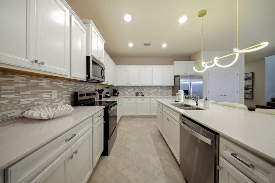 Welcome to this bright kitchen featuring sleek white cabinetry and a spacious island, ideal for your culinary adventures. With modern appliances and a stylish tile backsplash, this space invites you to create and enjoy delicious.