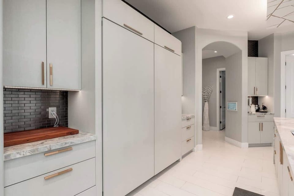 Bright, modern kitchen awaits with gleaming white cabinetry, marble countertops, and warm wood accents. You'll love the sleek tile backsplash and open flow into adjoining spaces, perfect for your culinary adventures.