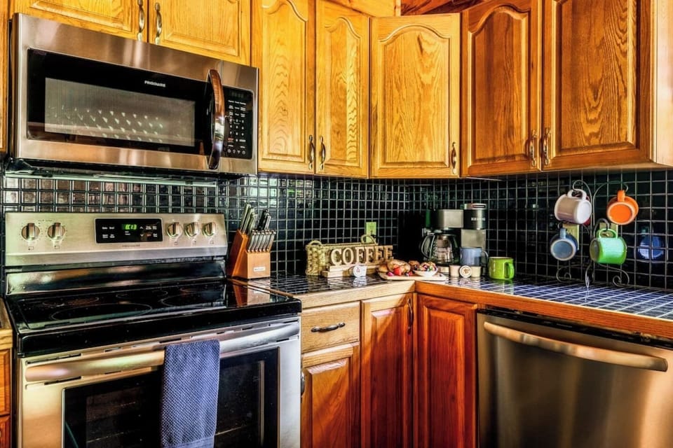 Kitchen appliance detail showing stainless steel range, built-in microwave, dishwasher, and hanging coffee mugs for your morning brew