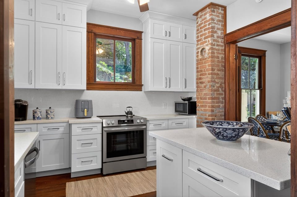 Sunlit shaker kitchen with quartz, stainless range, and exposed brick chimney