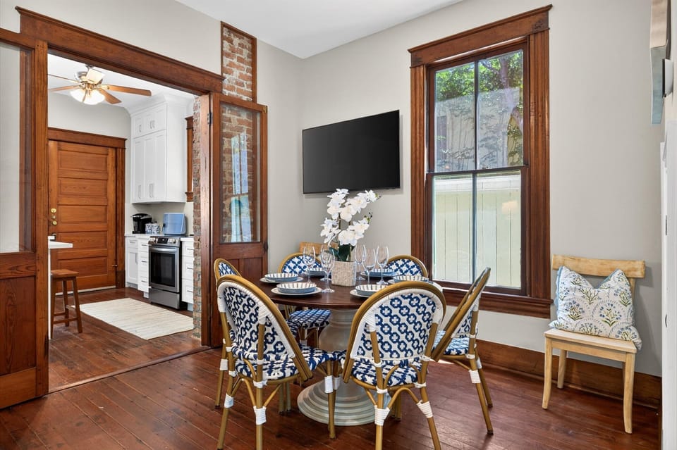 Sunny dining area with TV, bistro chairs, and access to a modern kitchen